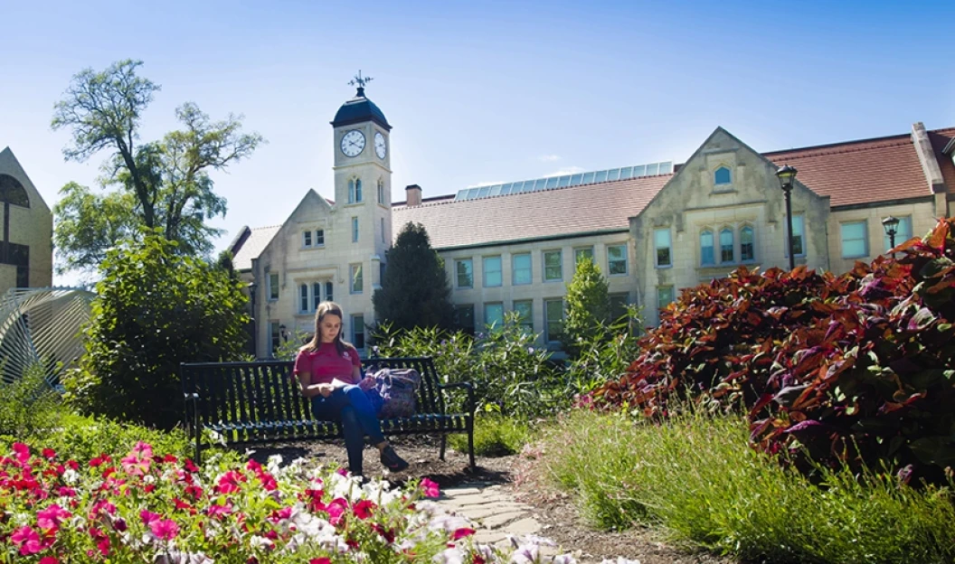 Bradley University Campus in the spring time. Female student surrounded by flourishing plants, studying her university books
