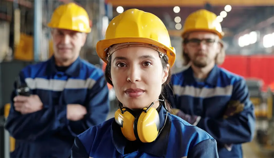 Female engineer in hardhat and safety gear in front of two male engineers inside a warehouse