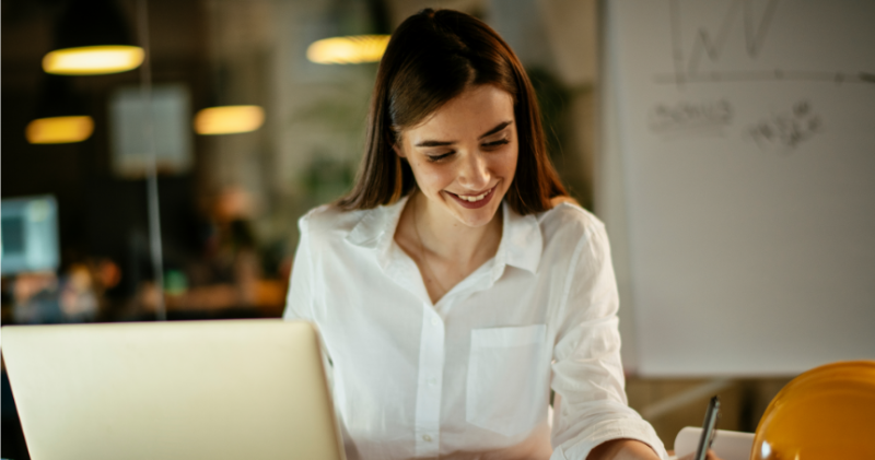 Woman working in front of laptop with whiteboard in background